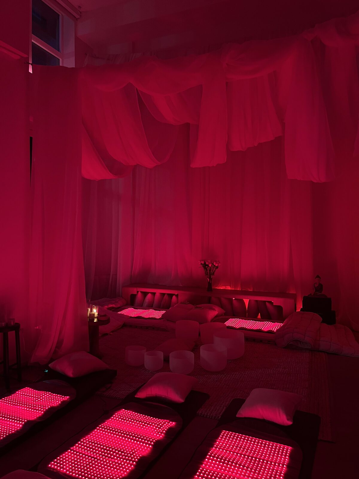 The PöP room at night — sheer canopy drapes, glowing red light therapy mats, crystal sound bowls, and low Japanese beds, all held in deep red light.